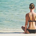 woman wearing bikini in yoga position facing sea