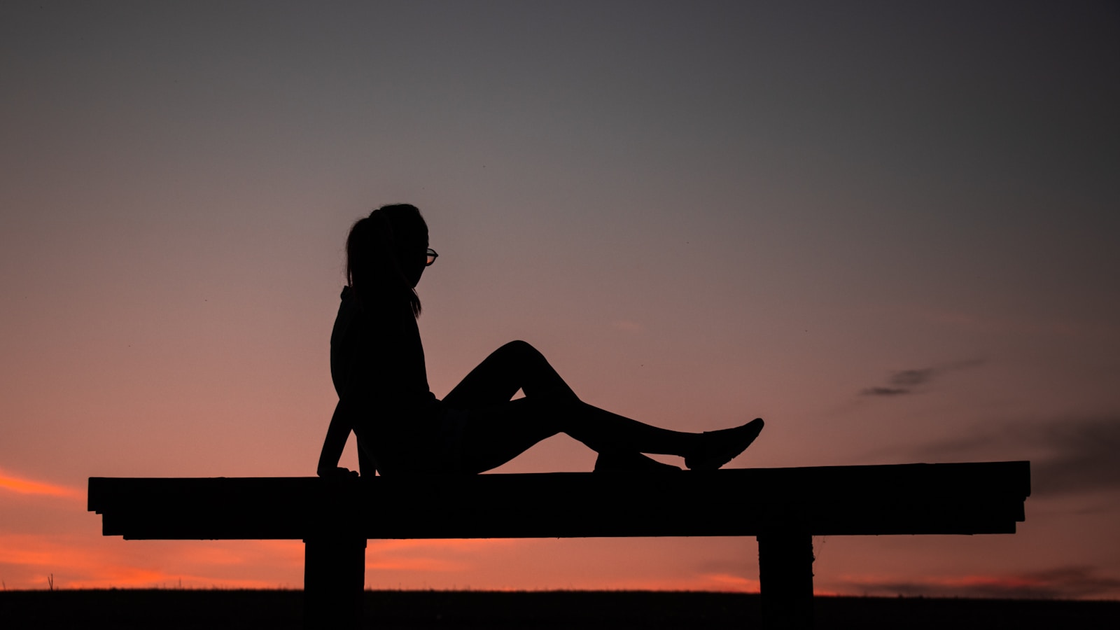 silhouette of woman sitting on brown wooden fence during sunset