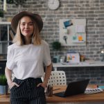 a woman standing in front of a desk with a laptop